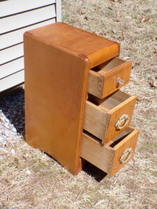 Vintage Art Deco Waterfall Nightstand End Table with 3 dovetailed drawers, the top having a glass knob and the lower 2 have ornate metal pulls. Beautiful Walnut wood with incised details Dimensions: 11" wide x 16" deep x 28" high